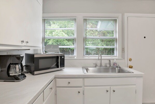 A kitchen with white cabinets, a microwave, a coffee maker, and a sink. - Central Midtown Cottage (Mobile)