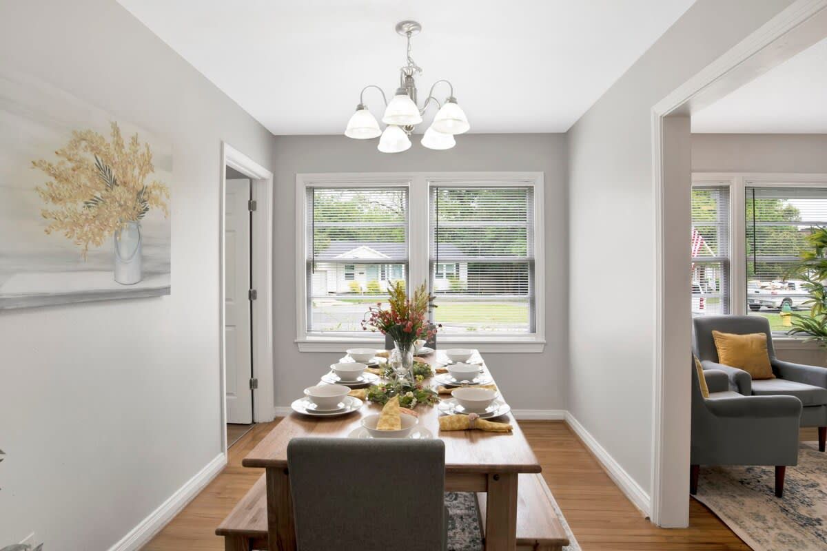 A dining room with a wooden table set for a meal, a chandelier, and a view through the windows.