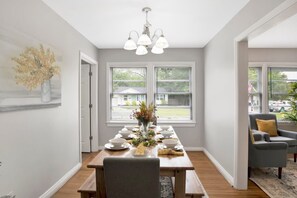 A dining room with a wooden table set for a meal, a chandelier, and a view through the windows. - Central Midtown Cottage (Mobile)