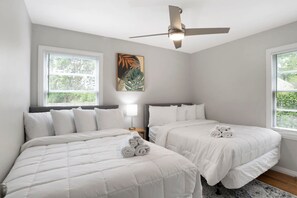 A hotel room with two beds, a ceiling fan, a window with blinds, a wall-mounted lamp, and a framed picture. - Central Midtown Cottage (Mobile)
