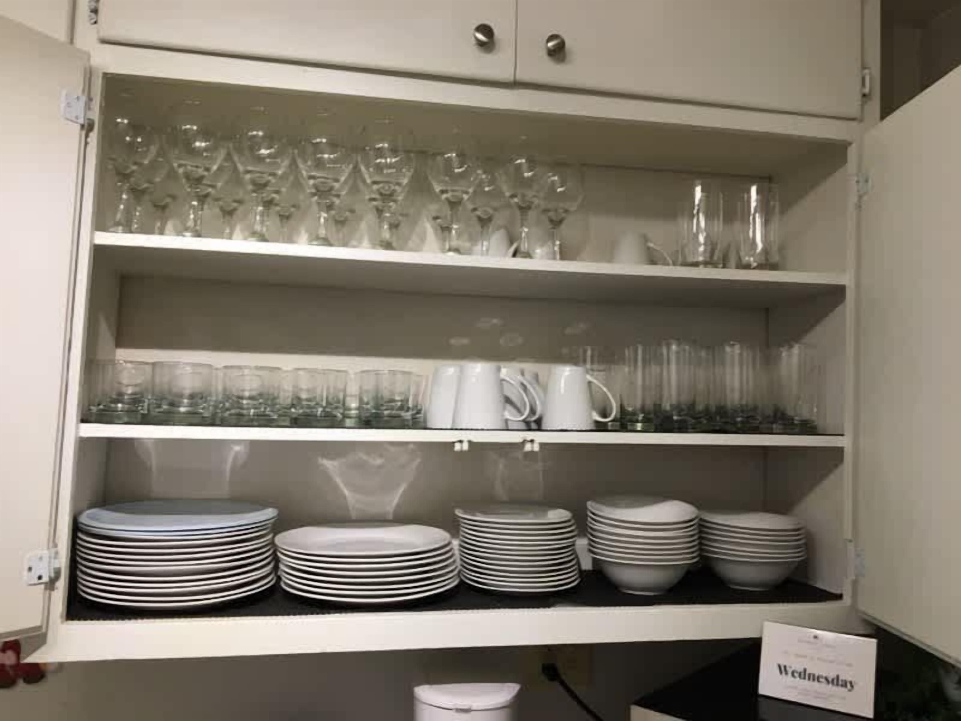 Un armario de cocina con repisas que contienen cristalería, platos y un cartel que indica 'Wednesday'.
