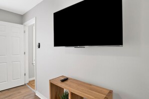 A room with a mounted flat-screen TV, a wooden console table with a remote, and a white door.
