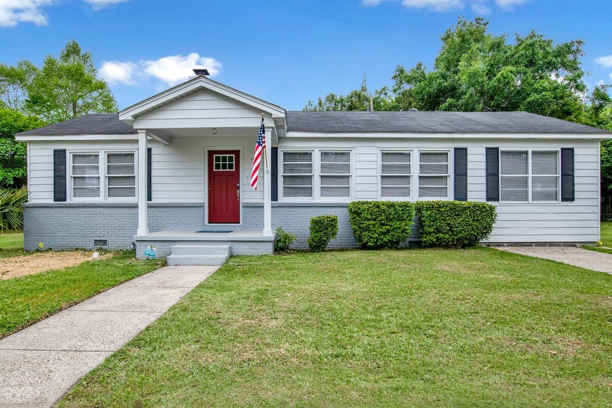 A single-story house with a red door, a front porch, and a small front yard.