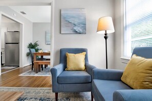 A modern living room with a blue armchair, a sofa, a lamp, and a painting on the wall. - Central Midtown Cottage (Mobile)