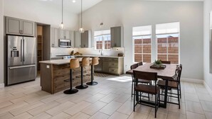 A modern kitchen with a central island, bar stools, and a dining table with chairs. - The Wanderer 2 Bedroom Home (Hurricane)