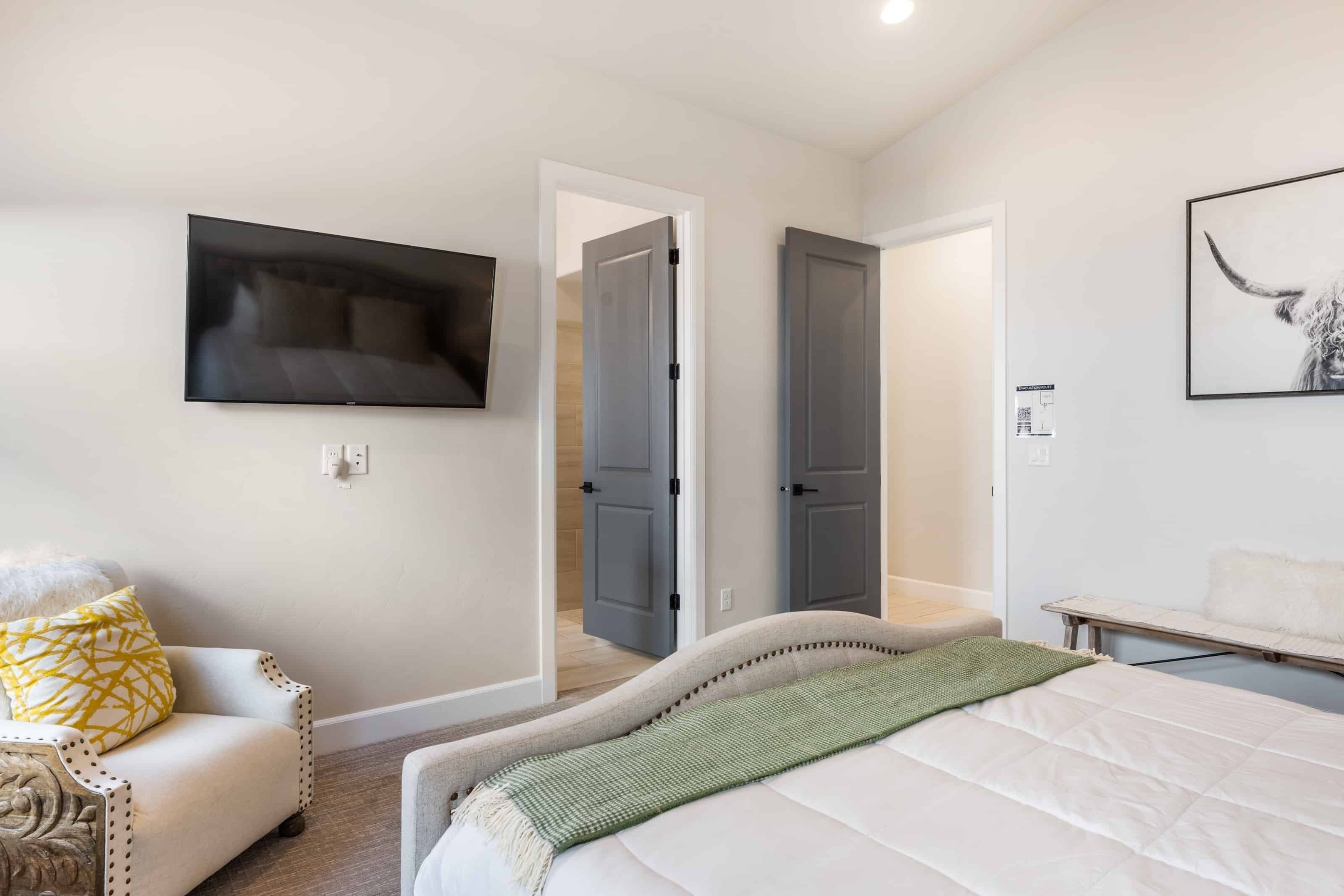 A bedroom with a bed, a chair, a TV, and two doors leading to other rooms.