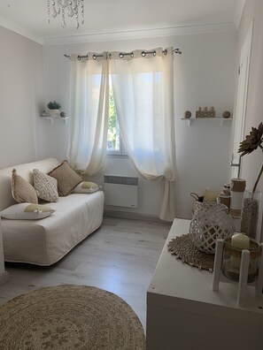 Ett mysigt vardagsrum med en vit soffa, en rund matta och ett vitt soffbord med dekorativa föremål.