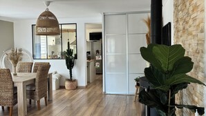 Een ruime woonkamer met een eethoek, een grote plant en een open haard.