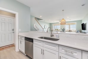 A modern kitchen with white cabinetry, a stainless steel dishwasher, and a large window providing natural light.