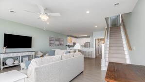 A modern living room with a sofa, a coffee table, and a TV. There is a staircase leading to another level. - Southern Belle: Oceanfront | Surfside Beach Vacation Rental (Surfside Beach)