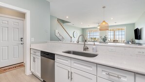 A modern kitchen with white cabinetry, a stainless steel dishwasher, and a large window providing natural light. - Southern Belle: Oceanfront | Surfside Beach Vacation Rental (Surfside Beach)