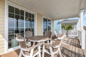 A covered outdoor patio with a round table and four Adirondack chairs. - Southern Belle: Oceanfront | Surfside Beach Vacation Rental (Surfside Beach)