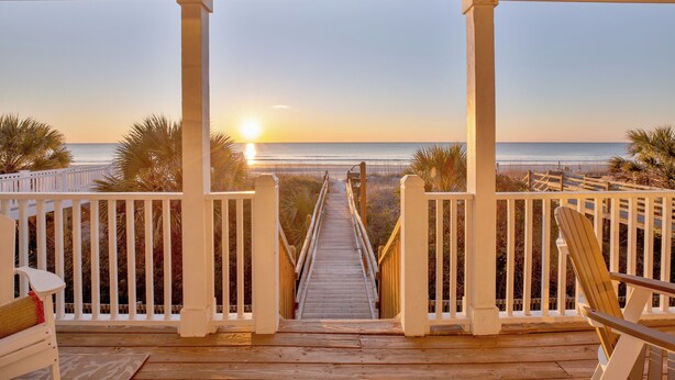 A wooden deck with a view of the sunset over the ocean, white railings, and a chair. - Southern Belle: Oceanfront | Surfside Beach Vacation Rental (Surfside Beach)