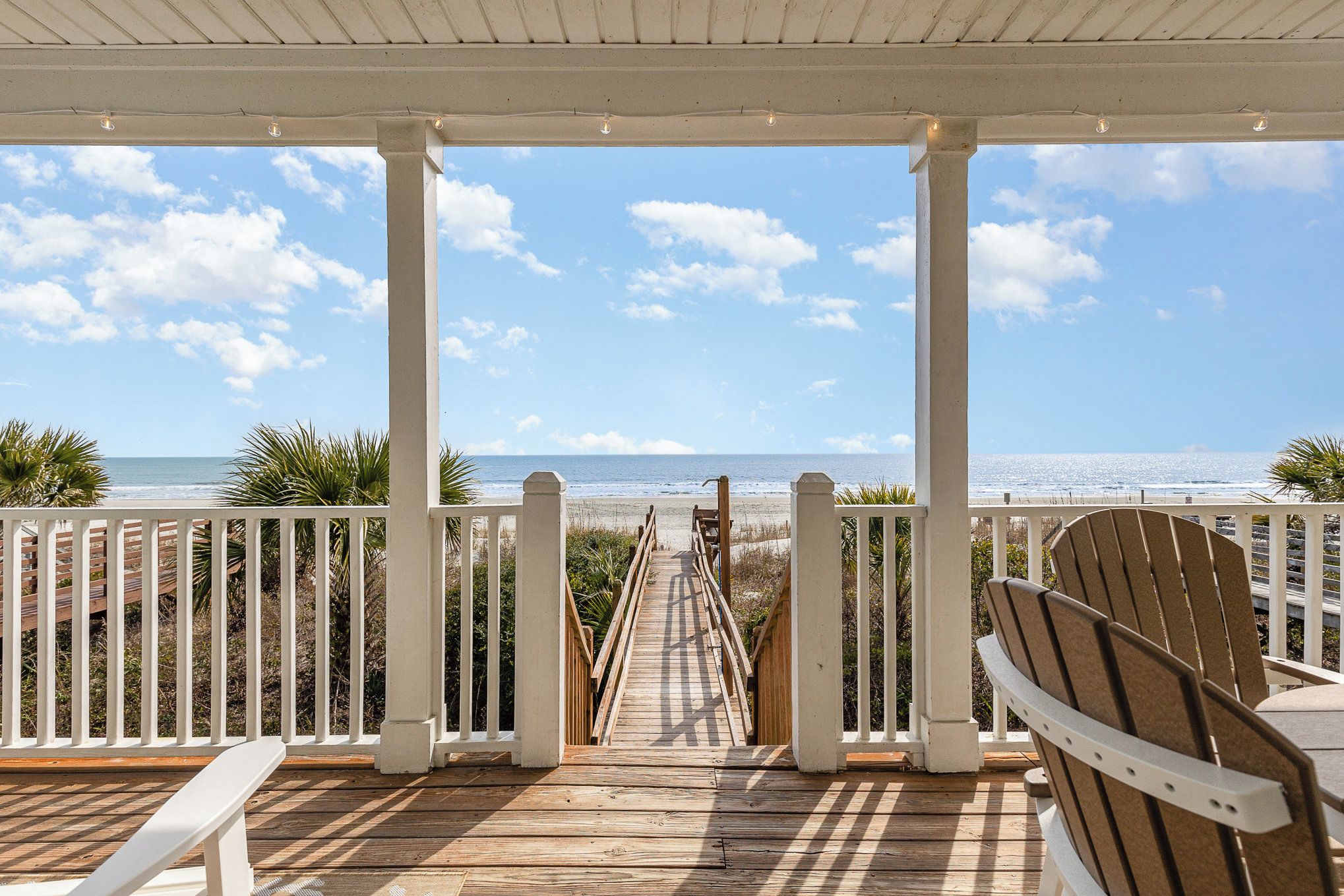 A wooden deck with a view of the beach, white railings, and a wooden chair.