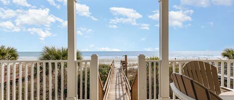 A wooden deck with a view of the beach, white railings, and a wooden chair.