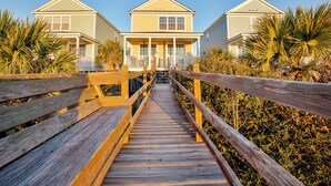A wooden boardwalk leading to a row of two-story beach houses with a covered porch and a clear blue sky. - Southern Belle: Oceanfront | Surfside Beach Vacation Rental (Surfside Beach)