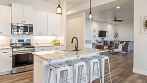 A modern kitchen with white cabinets, stainless steel appliances, a marble countertop, and bar stools.