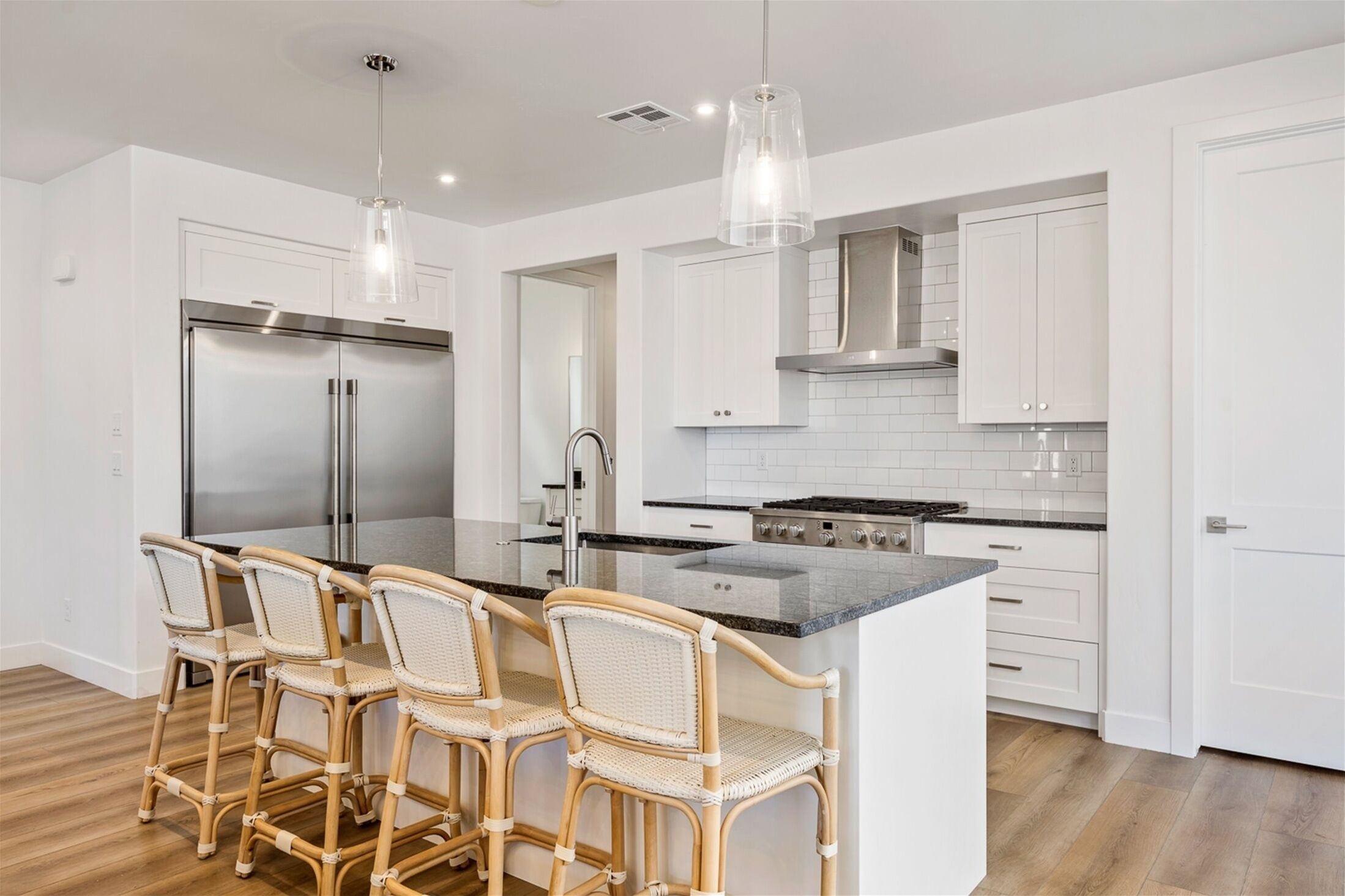 A modern kitchen with white cabinets, a stainless steel refrigerator, a gas stove, and a central island with bar stools.
