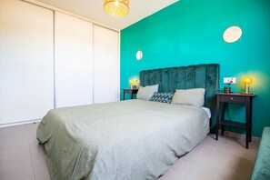 A bedroom with a bed, two bedside tables, a nightstand, a wall-mounted lamp, and a ceiling light fixture.