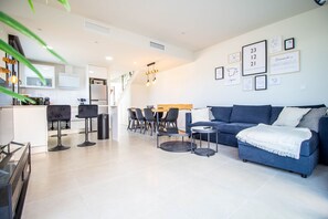 A modern living room with a sofa, chairs, a coffee table, and a kitchen area with a refrigerator and cabinets.