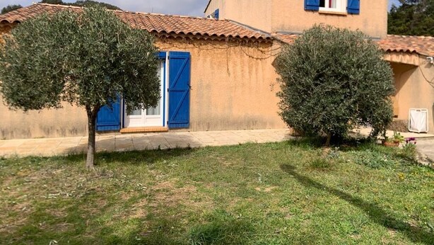 Un bâtiment à deux étages, doté d’un toit en tuiles, de volets bleus et d’un petit jardin agrémenté de deux arbres.