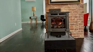 Een woonkamer met een open haard van baksteen, een lijstwerk schilderij en een lamp op een bijzettafeltje.