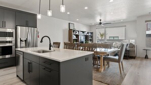 A modern kitchen with stainless steel appliances, a central island, and a dining area with wooden furniture. - Lula Inez Game Paradise 4 Bedroom Townhouse (St. George)