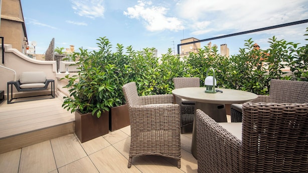 Un patio al aire libre con mobiliario de mimbre, una mesa redonda y plantas en macetas.
