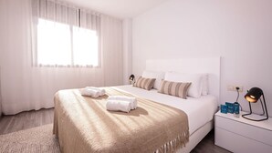 A hotel room with a large bed, a bedside table with a lamp, and a window with sheer curtains.