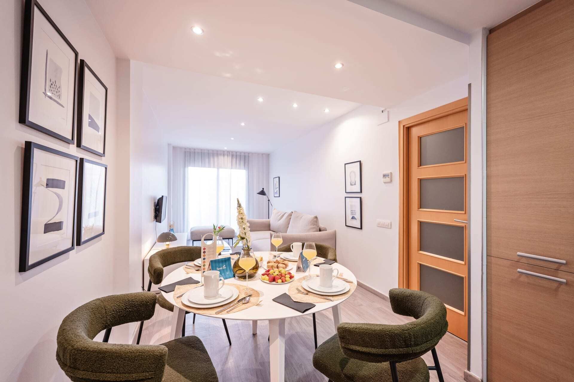 A dining area with a round table set for four, surrounded by green upholstered chairs.