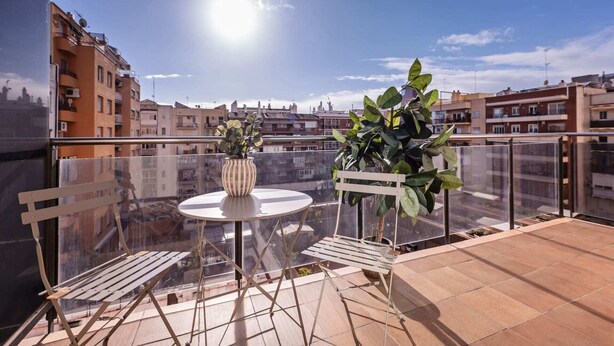 A balcony with a round table and two chairs, a potted plant, and a view of the cityscape.