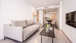 Ein modernes Wohnzimmer mit einem grauen Sofa, einem schwarzen Couchtisch und einem Essbereich mit Tisch und Stühlen.