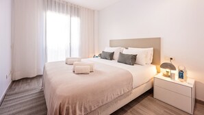 Ein Hotelzimmer mit einem großen Bett, einem Nachttisch, einer Lampe und einem Fenster mit Vorhängen.