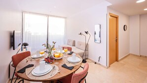Un coin repas avec une table ronde dressée pour quatre personnes, agrémentée d’assiettes, de couverts et d’un panier de fruits.