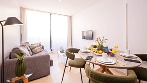 Un salon moderne avec un canapé, une table à manger dressée pour le petit-déjeuner et un téléviseur fixé au mur.