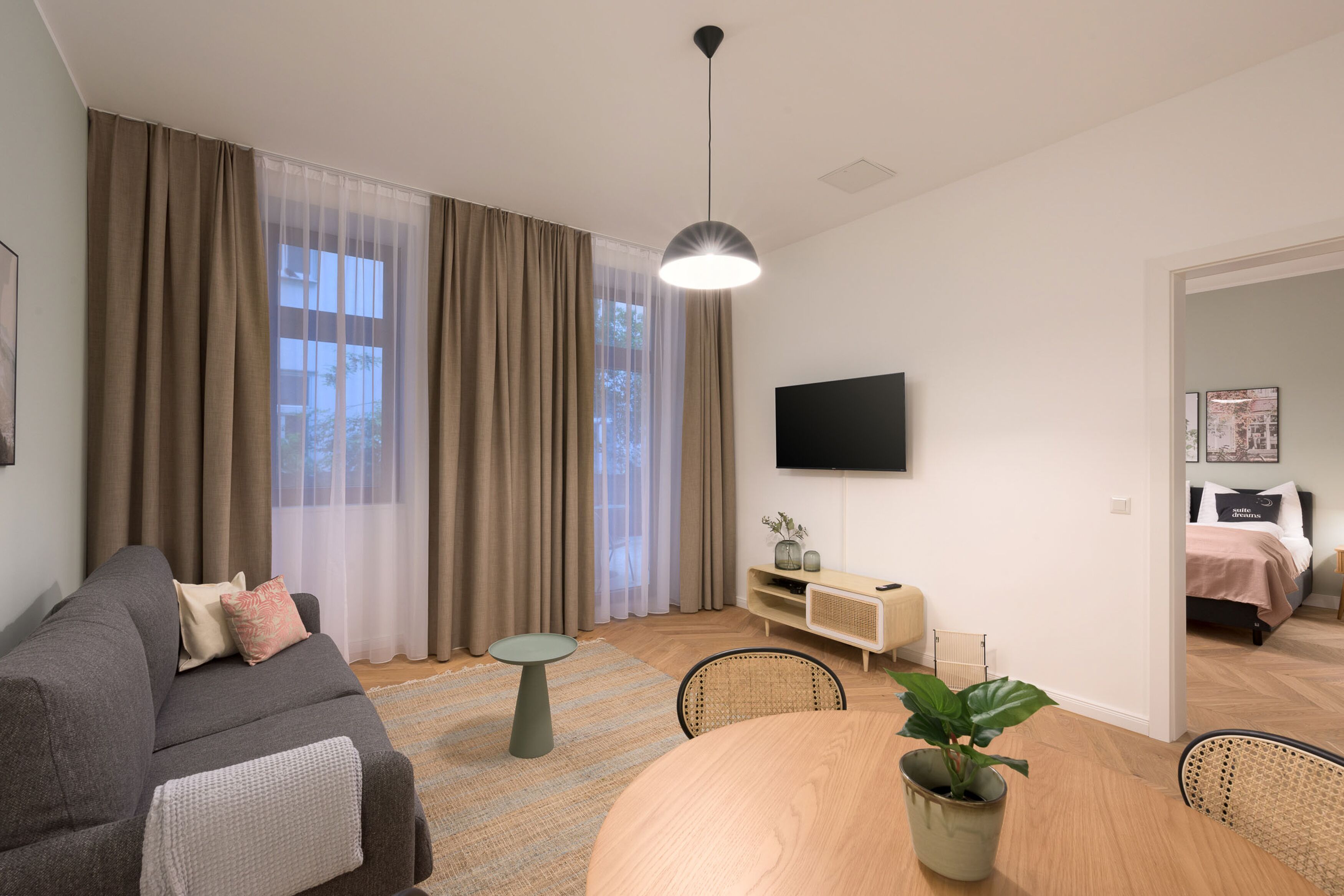 En moderne stue med sofa, spisebord og tv ophængt på væggen.