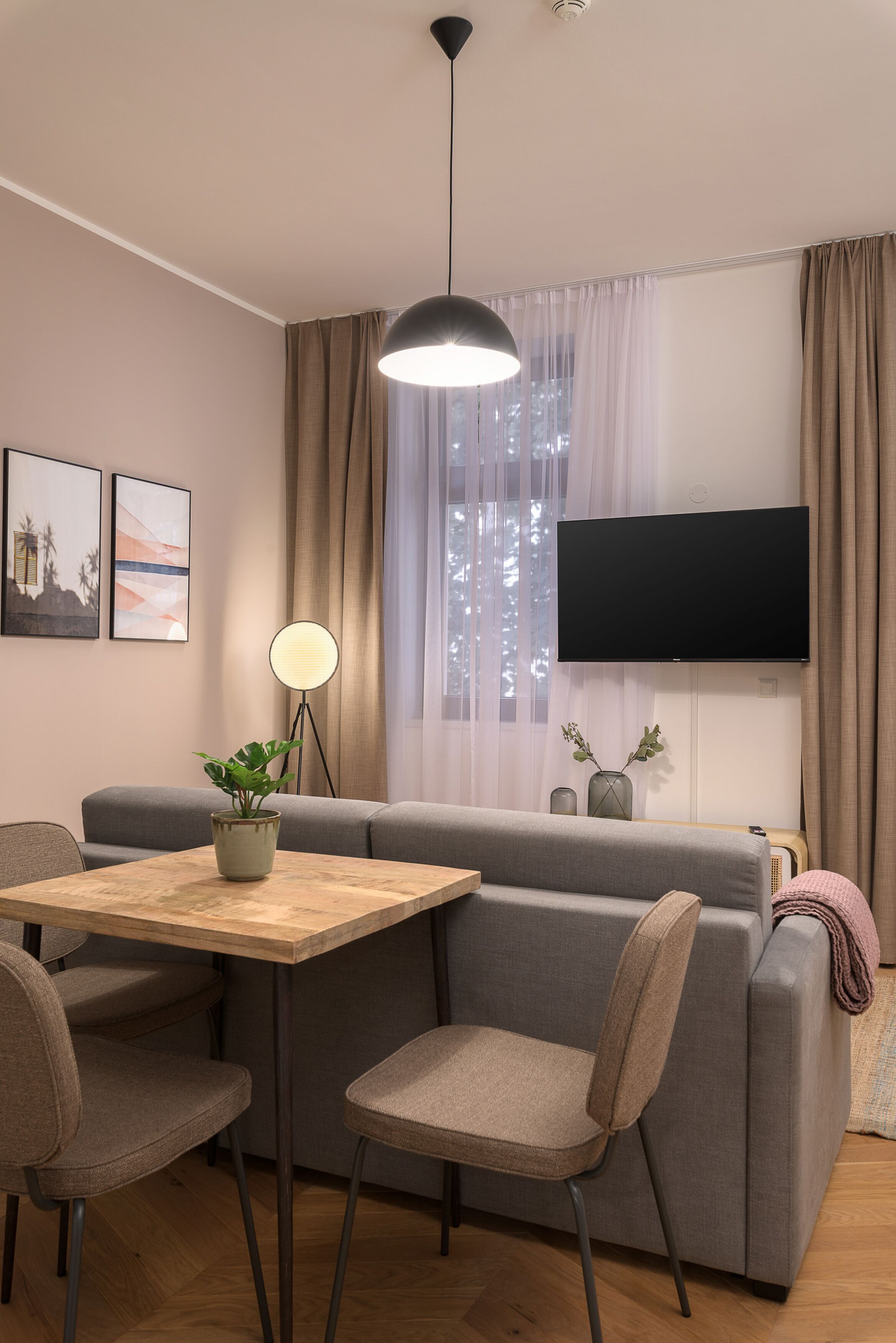 Ein modernes Wohnzimmer mit einer Couch, einem Esstisch mit Stühlen, einer Stehlampe und einem flachbildfernseher an der Wand.