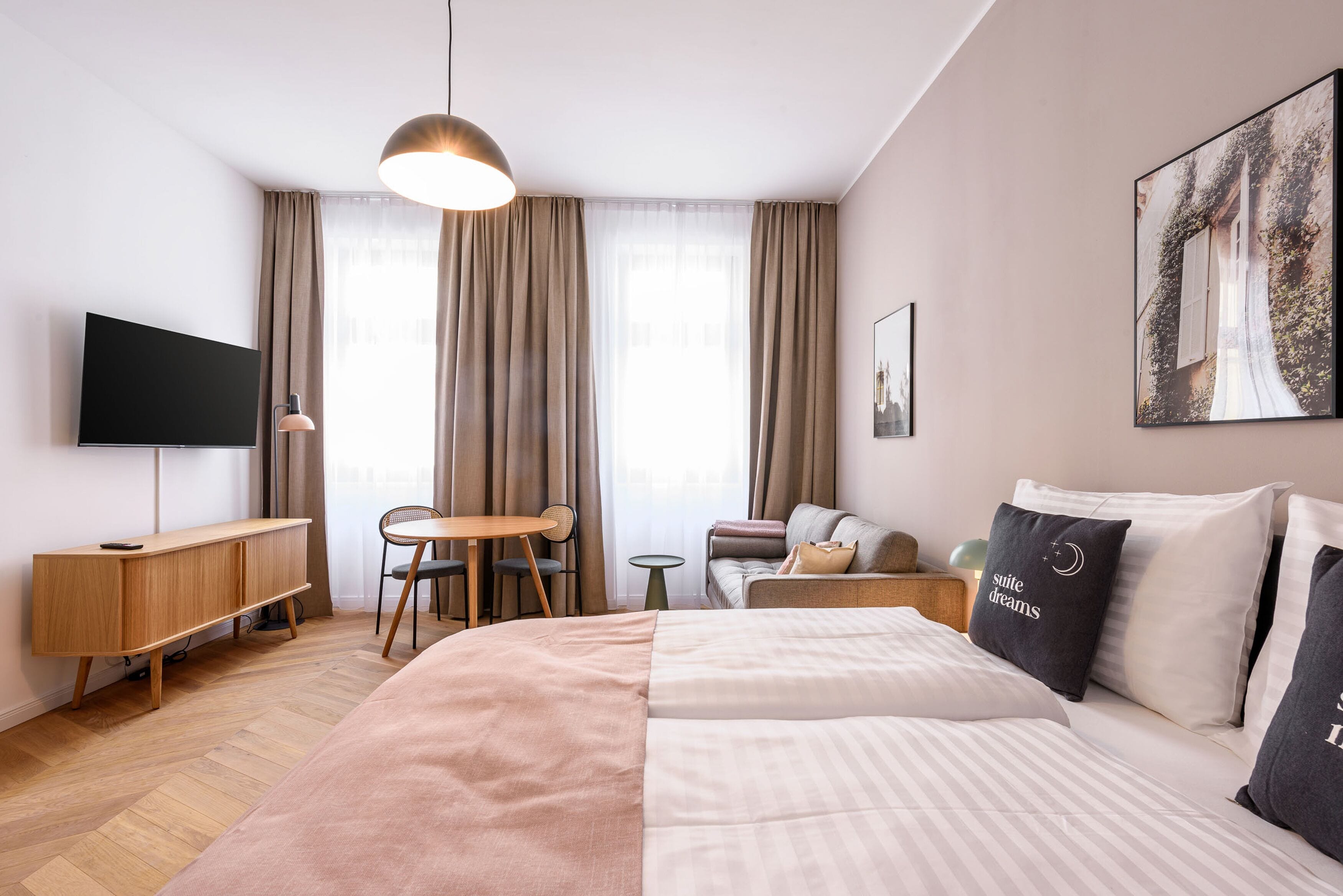 A hotel room with a bed, a desk, a chair, a TV, and a painting on the wall.