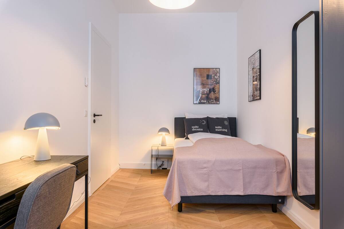 Une chambre à coucher avec un lit, des lampes de chevet, un bureau avec une lampe, une chaise et un miroir.