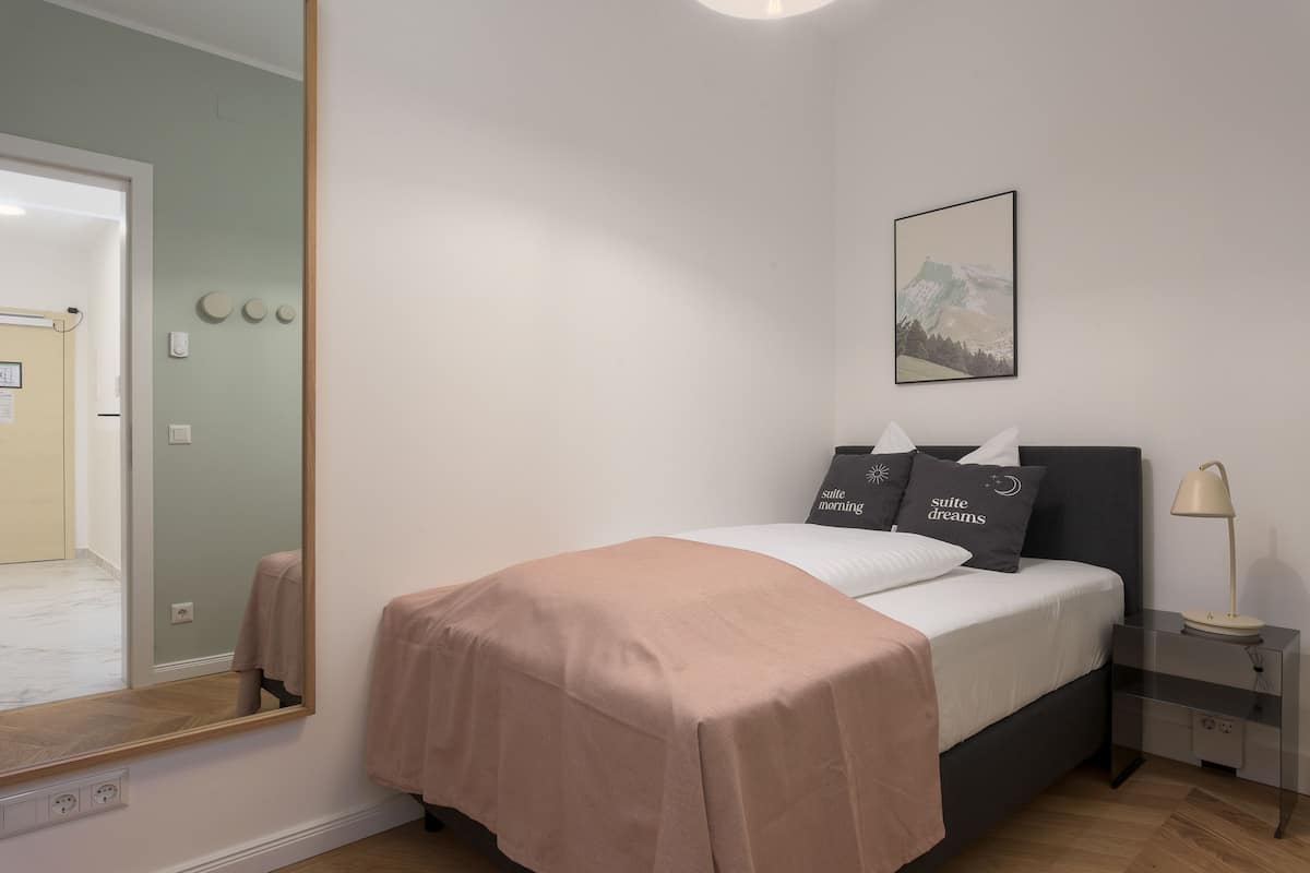 Une chambre à coucher bien rangée, avec un lit, une table de chevet, une lampe et un grand miroir.