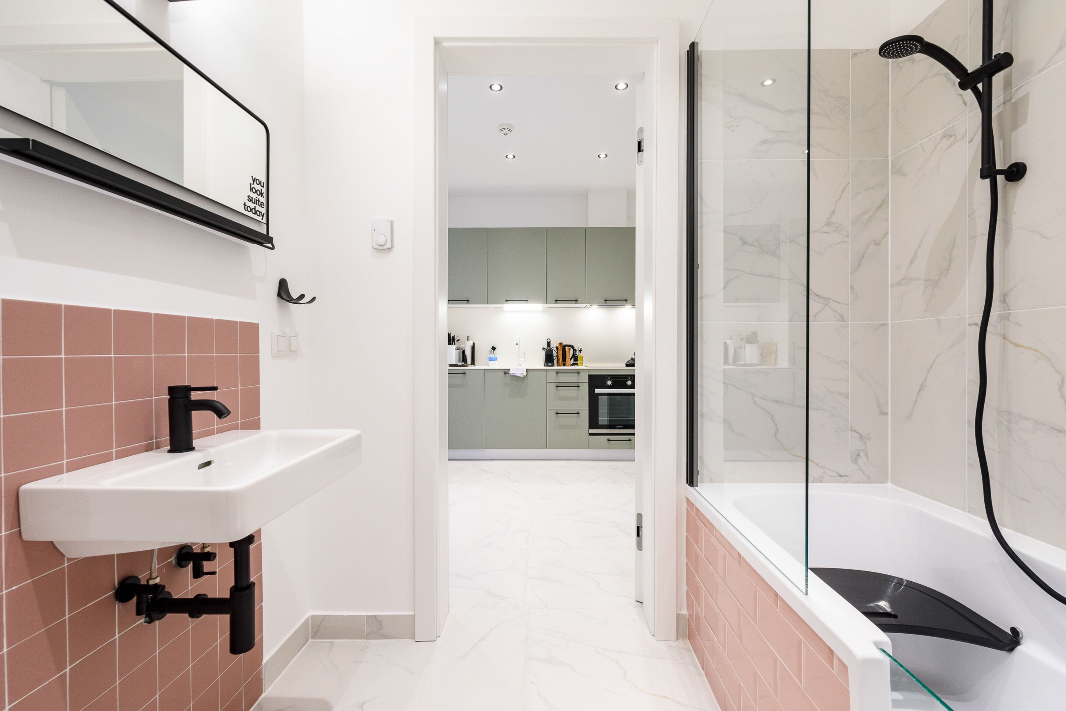 Een moderne badkamer met een douchecabine van glas, een witte wastafel met een zwarte kraan, en een spiegel boven de wastafel.