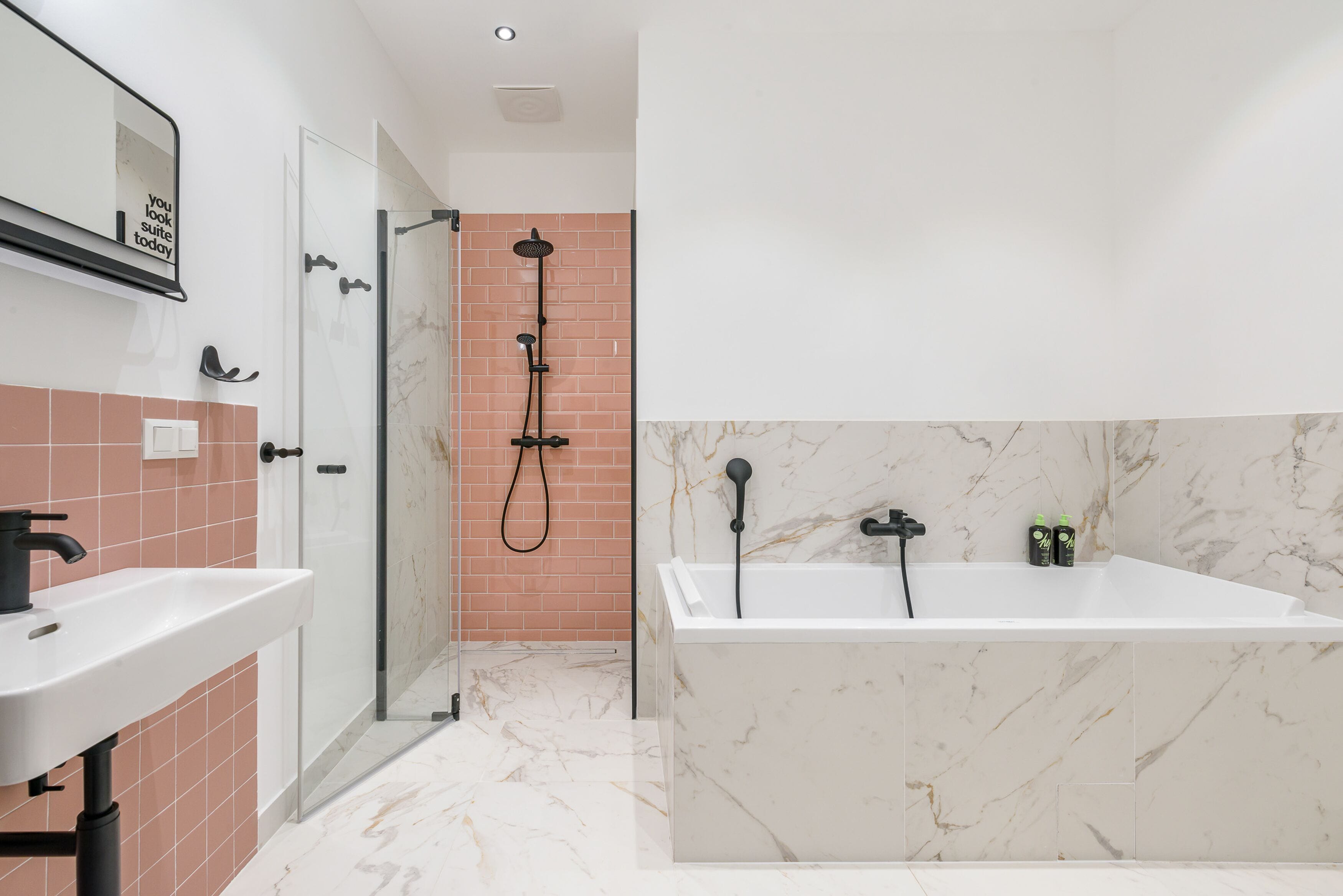 A modern bathroom with a white sink, a glass-enclosed shower, and a marble-tiled bathtub.