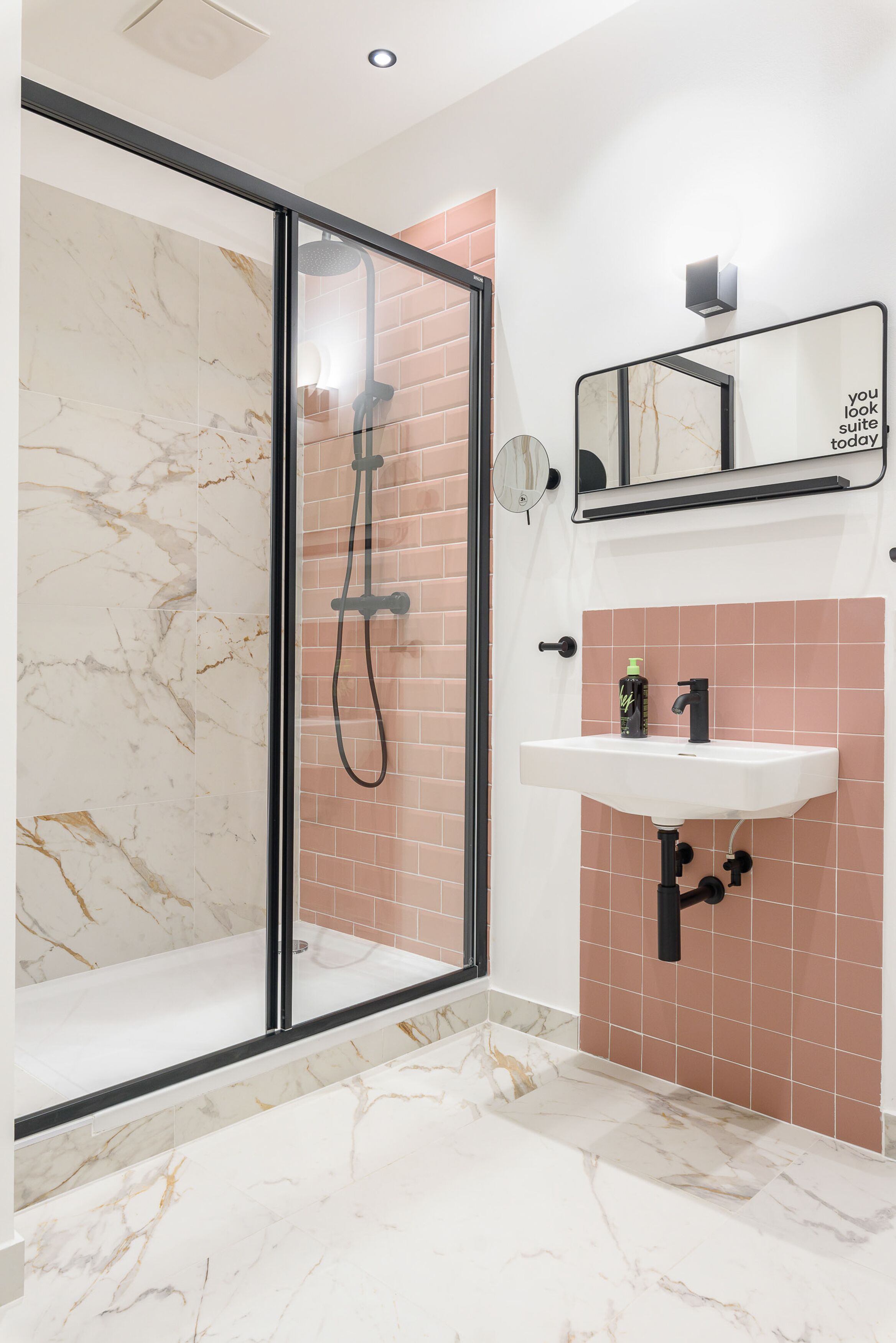 Un baño con cabina de ducha de vidrio, un lavamanos con espejo y paredes de azulejos rosas.