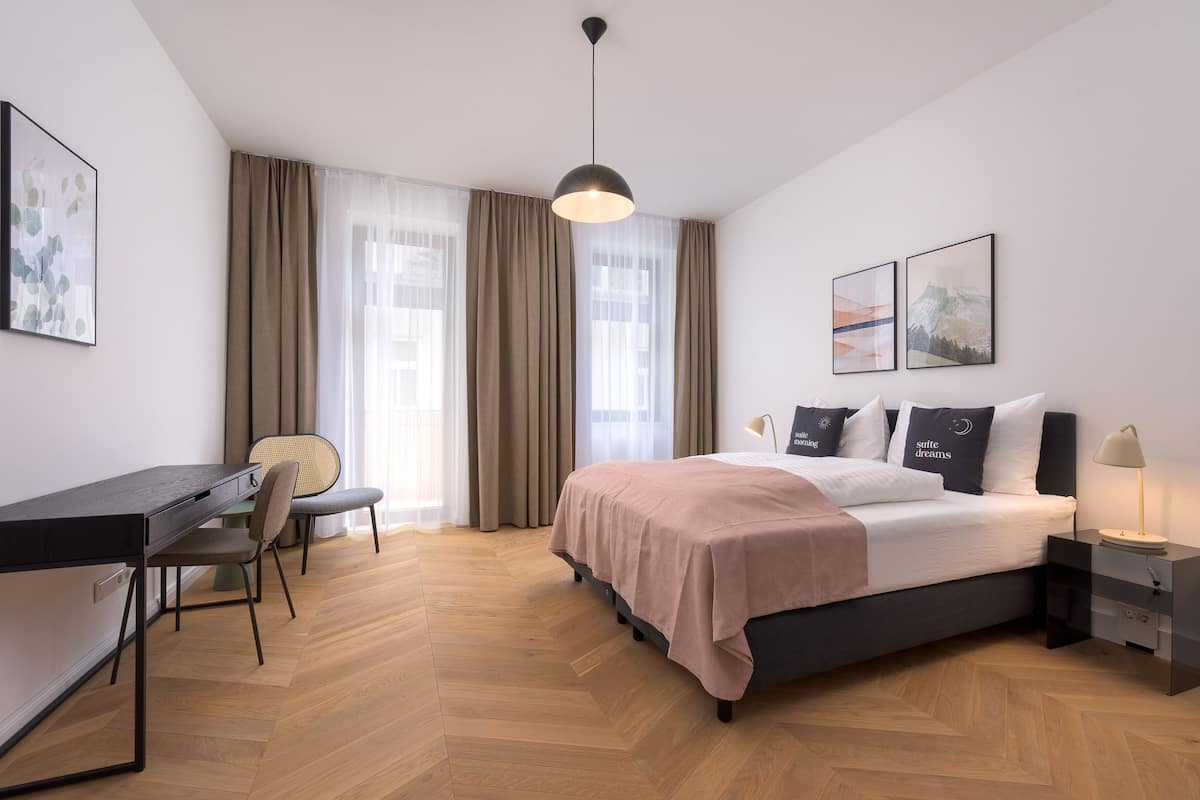 Une chambre à coucher moderne avec un lit, un bureau, une chaise et une table de chevet avec une lampe.