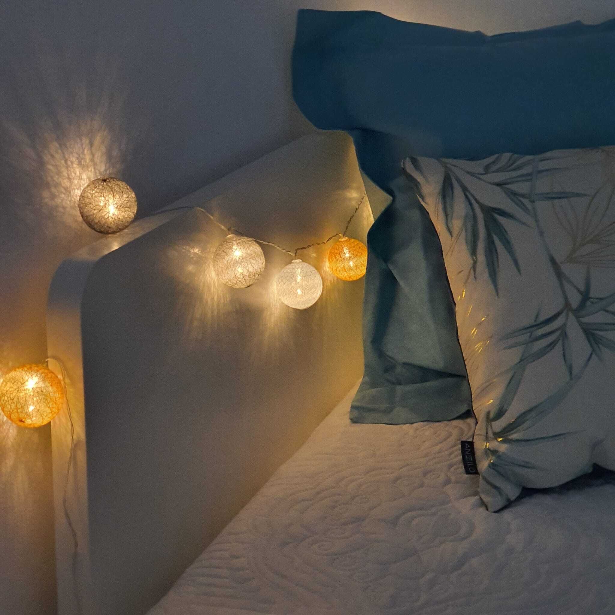 Un dormitorio con cama, almohadas e iluminación tenue en la cabecera.
