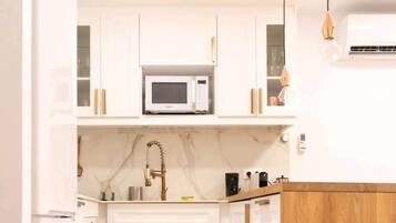 A compact kitchen with white cabinets, a microwave, a sink with a vintage faucet, and a patterned tile floor.