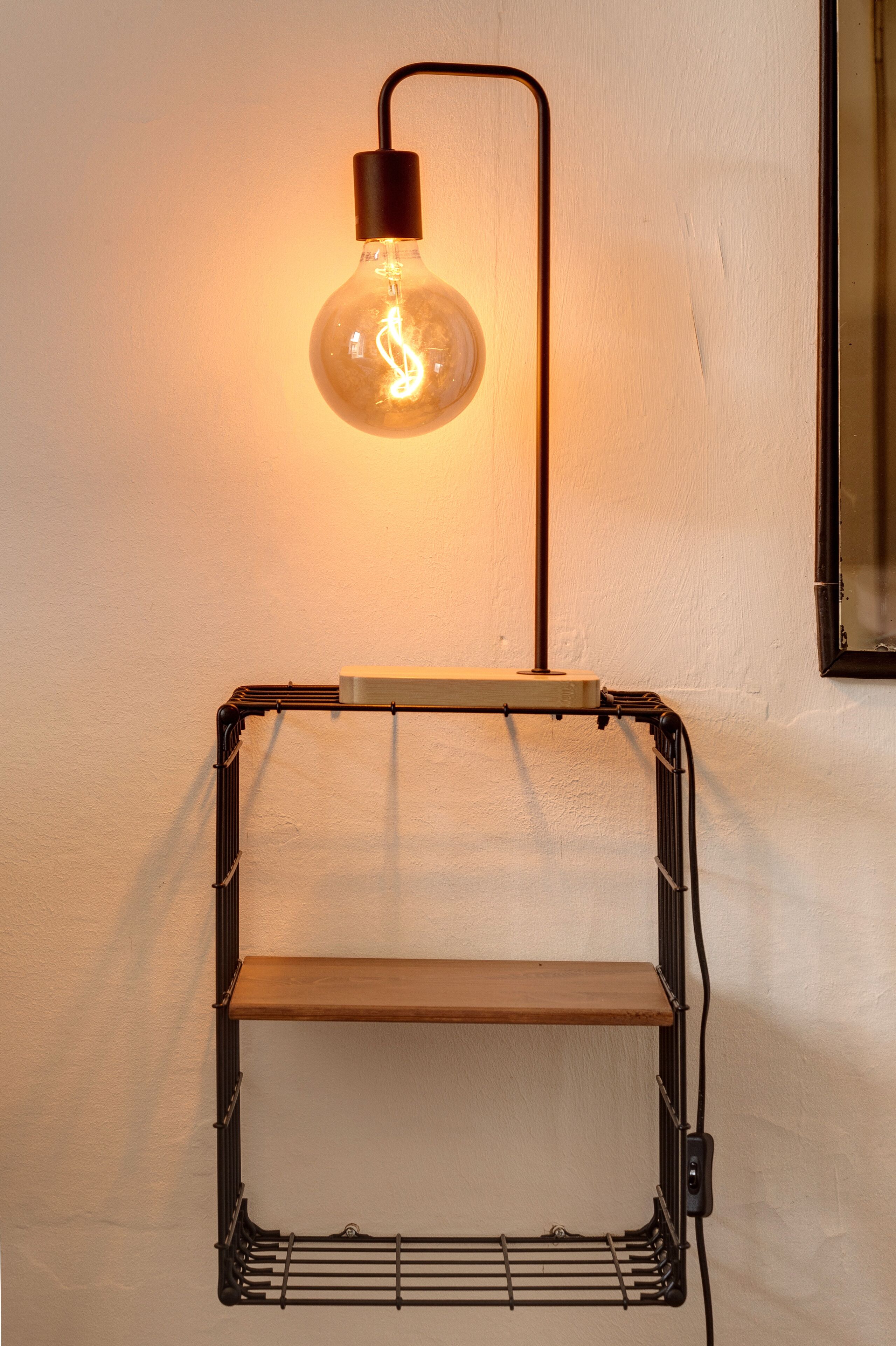 Une étagère métallique fixée au mur, avec une seule ampoule placée au-dessus.