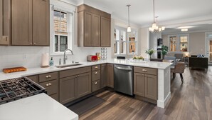 A modern kitchen with brown cabinets, a stainless steel dishwasher, and a white countertop. - Seabrook Salt and Vine | Pet Friendly, Fire Pit, Single Level, EV Charger, 3BR (Pacific Beach)