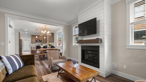 A modern living room with a fireplace, a television mounted on the wall, and a dining area in the background. - Seabrook Salt and Vine | Pet Friendly, Fire Pit, Single Level, EV Charger, 3BR (Pacific Beach)