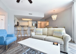 A modern living room with a sofa, a coffee table, and a dining area with chairs and a kitchen in the background.